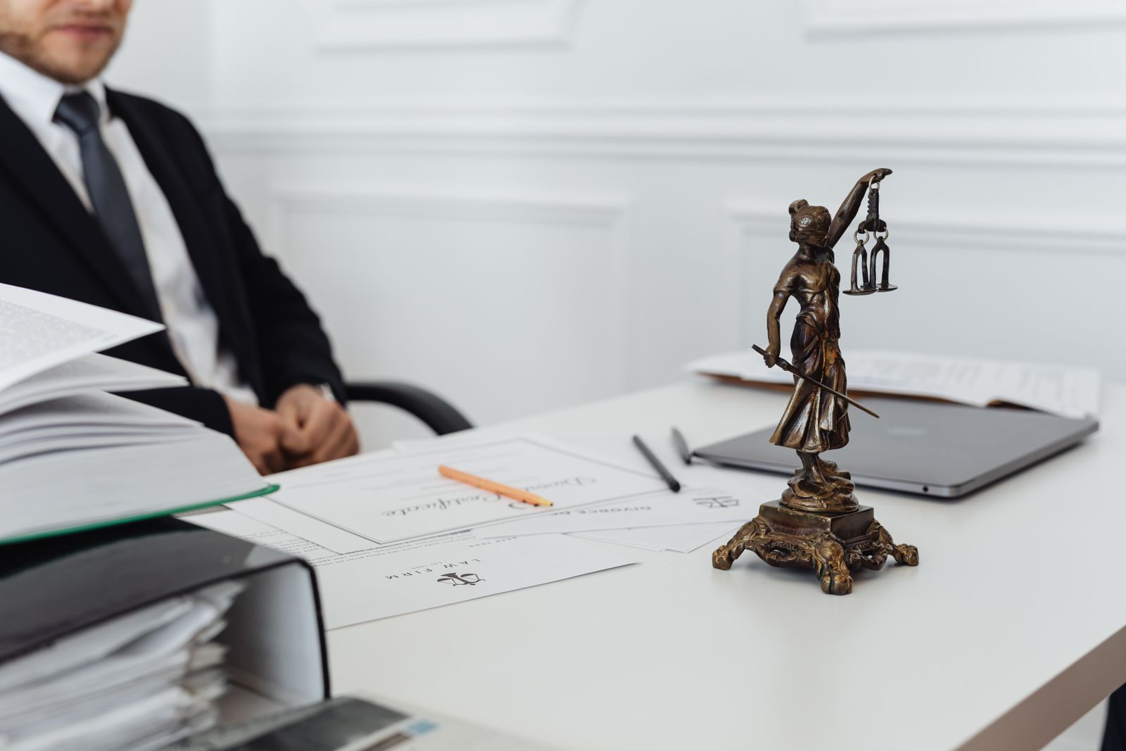 Espace de travail d'un professionnel du droit avec une statue de la Justice, des documents et un ordinateur portable.